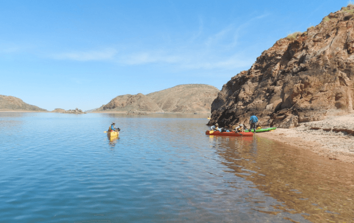 Outdoor education example of a wide image shot of students canoeing outdoors on a river with blue sky in the background.